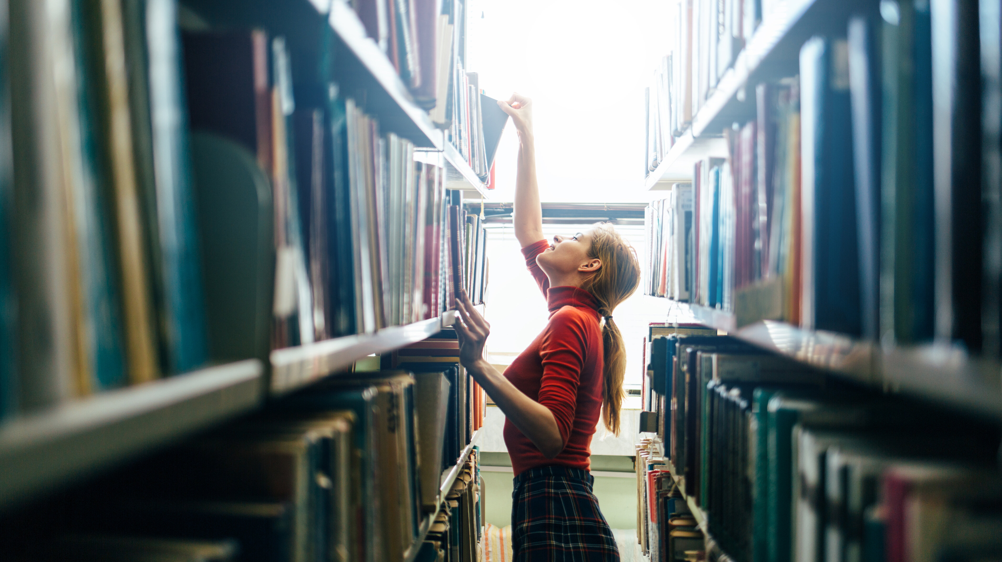 Frau sucht ein Buch in einem regal in der Bibliothek