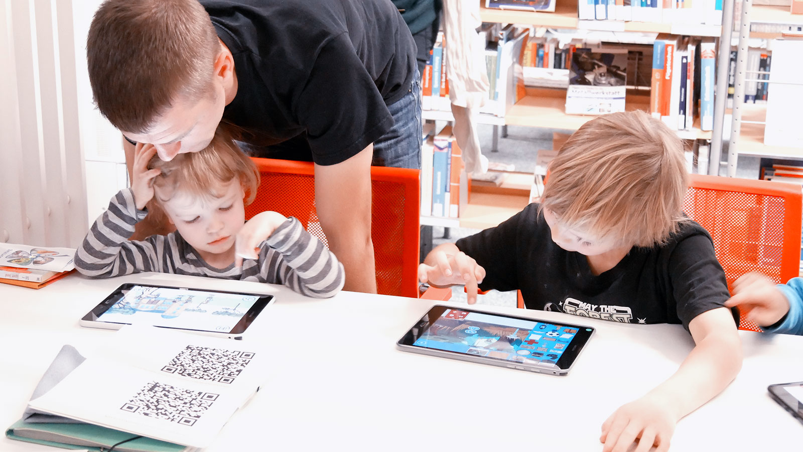 Kinder spielen mit Tablet, beobachtet von Elternteil